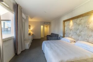 A bright hotel room with a double bed and a sofa.